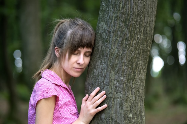 夏の森の木の幹にもたれて若い女性。