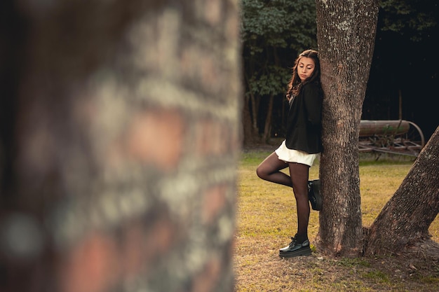 Young woman leaning on a tree with trendy clothes