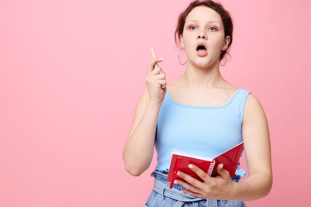 ノートブックとペンピンク色の背景を変更せずに学ぶ若い女性