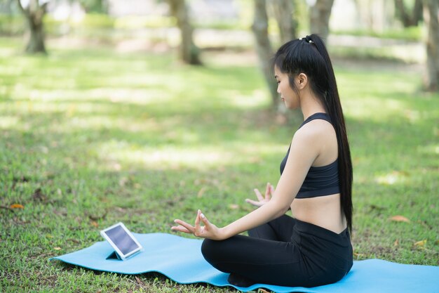 Giovane donna che impara l'esercizio di yoga in una videoconferenza all'aperto nel parco, concetto di yoga sportivo