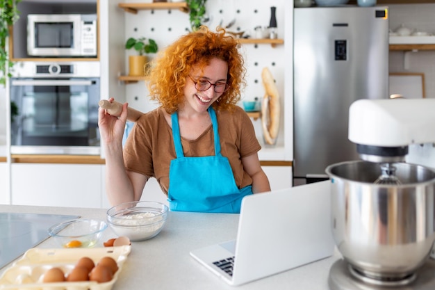 Una giovane donna impara a cucinare, guarda le video ricette su un laptop in cucina e cucina un piatto cooking at home concept