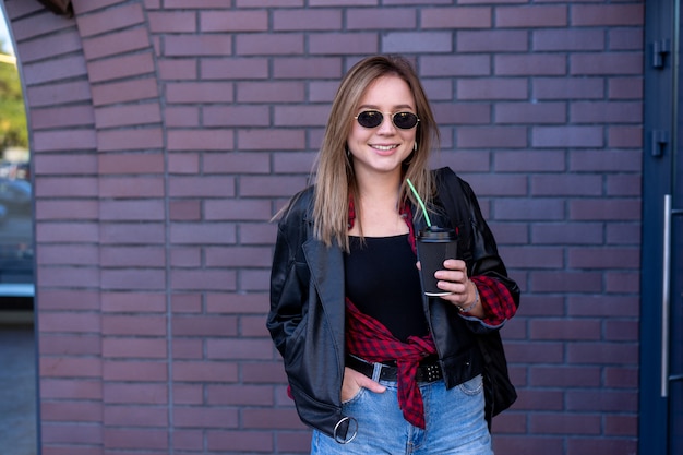 young woman in leather jacket having a drink on the street