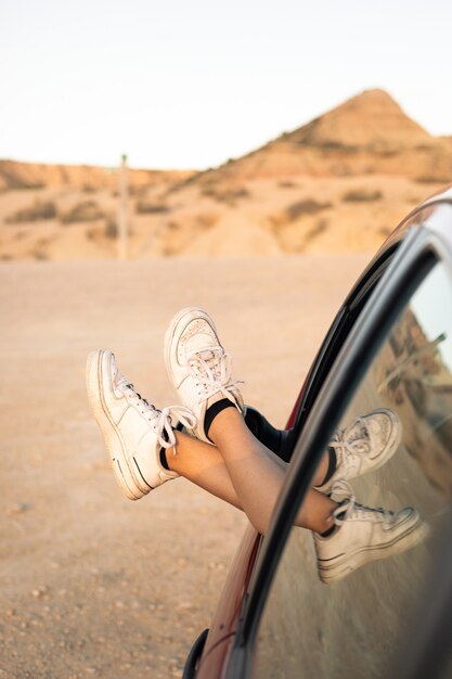 Young woman legs outside a car window in a dry landscape at Bardenas Reales, Navarra, Basque Country.