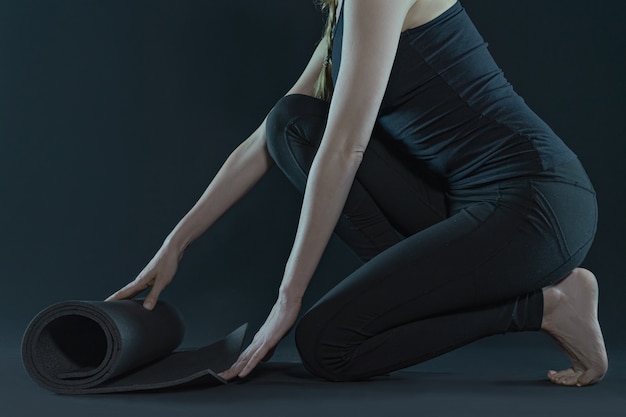 Young woman legs practicing yoga and yoga mat on a dark black background. copy space.