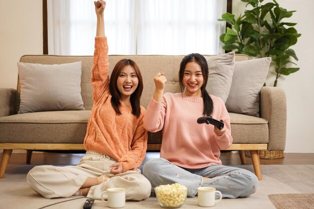 Young woman lesbian couple in sweater sitting on the floor and holding joystick to playing game