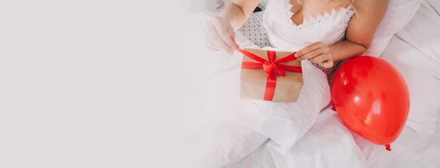 A young woman lies on the bed and opens a box with a gift celebration of Valentine's Day