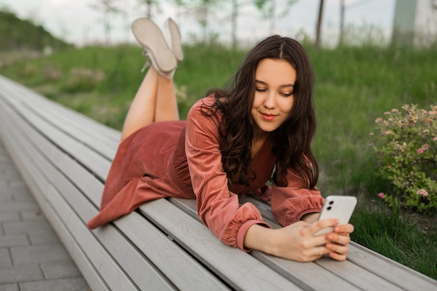 молодая женщина лежит на скамейке с мобильным телефоном