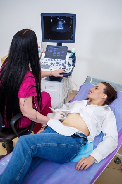 A young woman lies on a couch, a doctor appointment, an ultrasound scan of the abdominal organs is performed on the girl, the doctor examines the patient