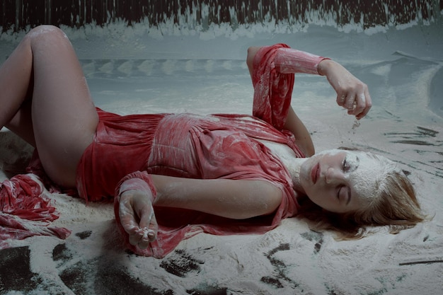 Young woman lies in flour on the floor and pours on the flour