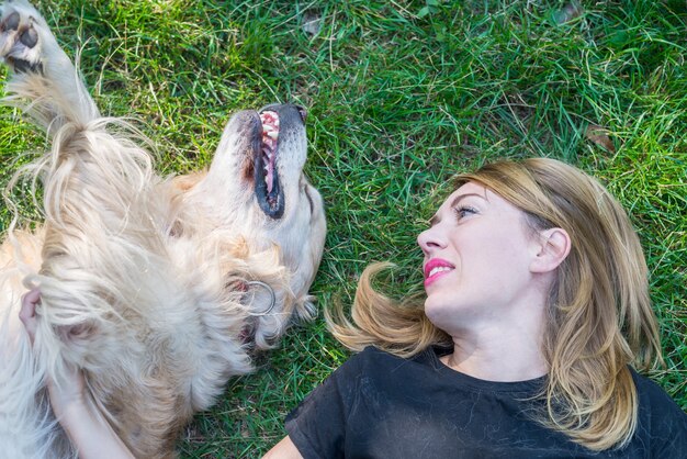 A young woman lies with a retriever dog on the lawn in the\
park. close-up.