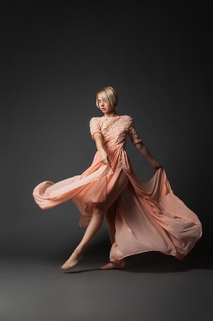 Young woman in light chiffon dress dancing on black plain .