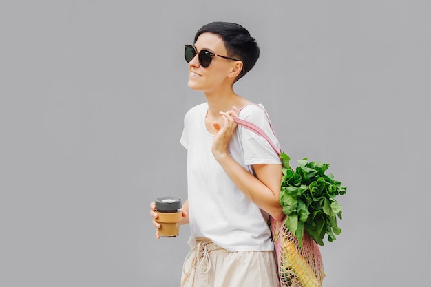 Giovane donna in abiti estivi leggeri con un sacchetto ecologico di verdure, verdure e una tazza da caffè riutilizzabile. stile di vita sostenibile. concetto ecologico.