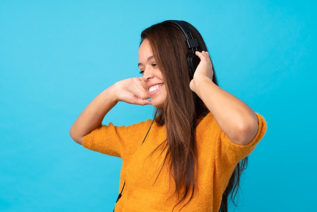 Young woman listening music over blue wall