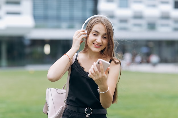 Young woman listening to music in headphone use smartphone at city walk look around