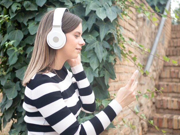 Photo young woman listening to music on headphones from playlist on cellphone