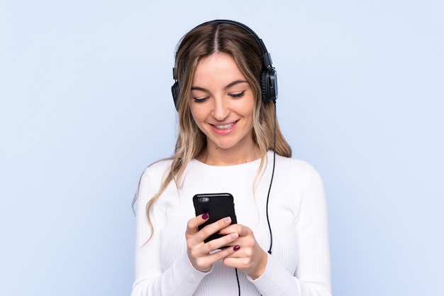 Young woman listening music over isolated wall