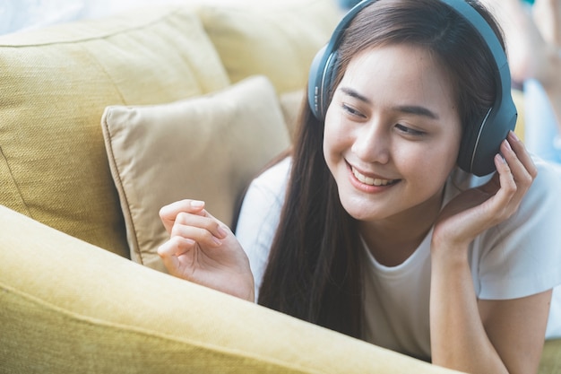 Young woman listening to music lying on sofa at home.