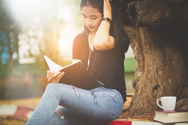 写真 ベンチで本を読みながら音楽を聴く若い女性