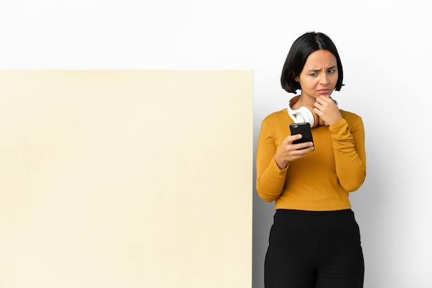 Young woman listening music with a big empty placard over isolated background thinking and sending a message