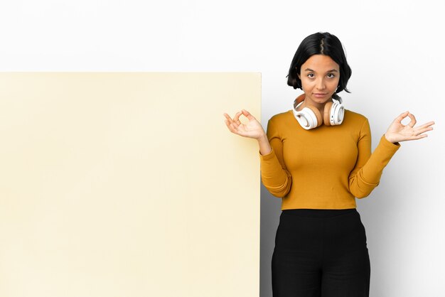 Young woman listening music with a big empty placard over isolated background in zen pose