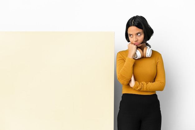 Young woman listening music with a big empty placard over isolated wall with tired and bored expression