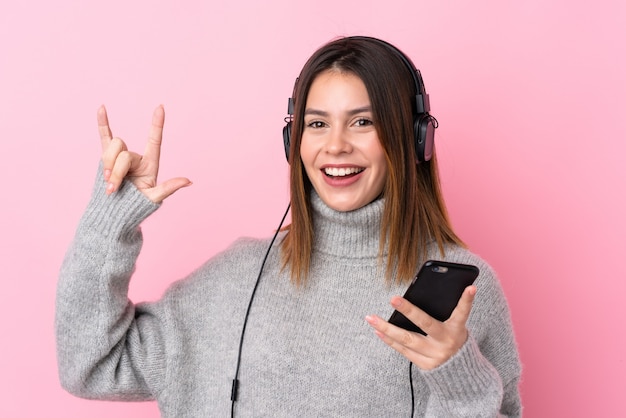 Musica d'ascolto della giovane donna con le cuffie sopra la parete rosa isolata