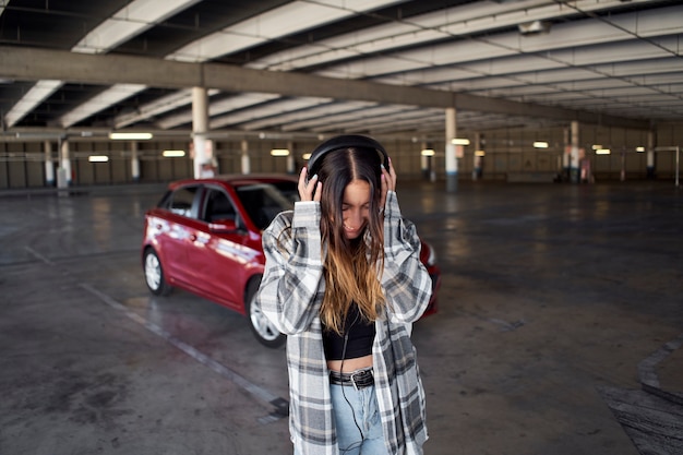 Giovane donna che ascolta la musica con le cuffie in un parcheggio. sta ascoltando musica con le cuffie.