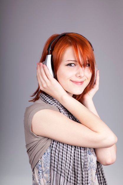 Young woman listening music with headphones. Portrait on grey background