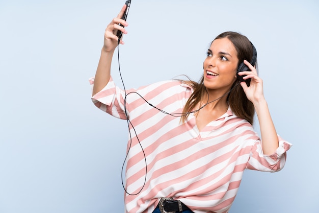 Young woman listening music with a mobile over isolated blue wall