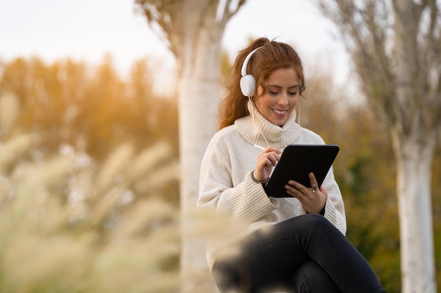 Young woman listening to music and writing on a digital tablet