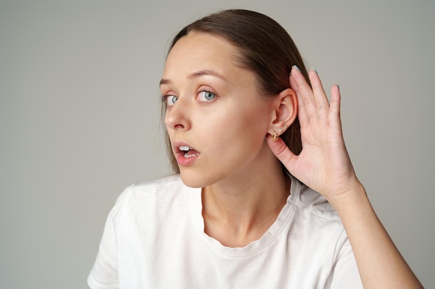 Фото Молодая женщина слушает с рукой на ухе на сером фоне