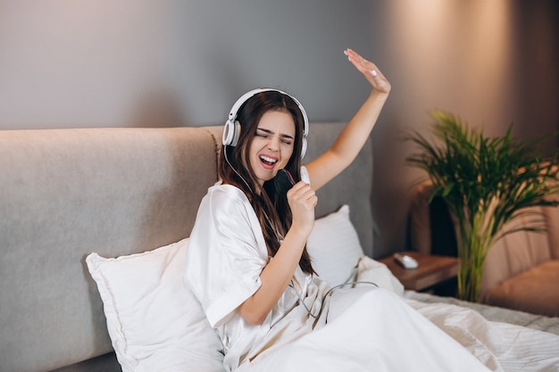 Young woman listens to music in bed. The brunette listens to music on headphones. The model sings songs and dances.