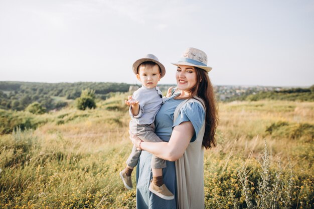 Giovane donna e ragazzino in un campo, all'aperto. madre che tiene suo figlio, sorridendo, entrambi con abiti vintage e cappelli di paglia.