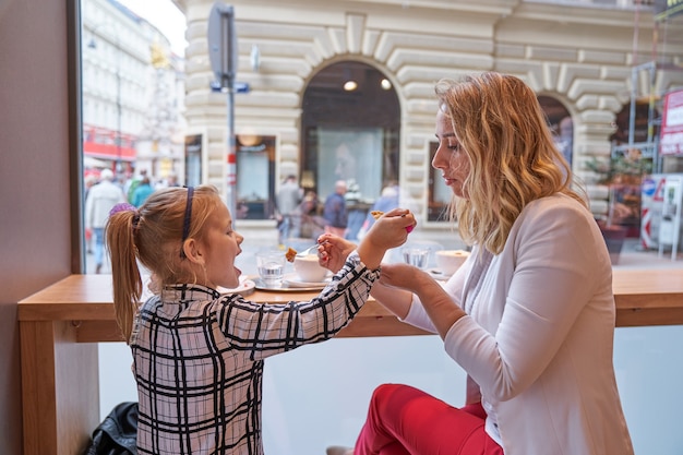 Молодая женщина и маленькая девочка едят торт в кафе