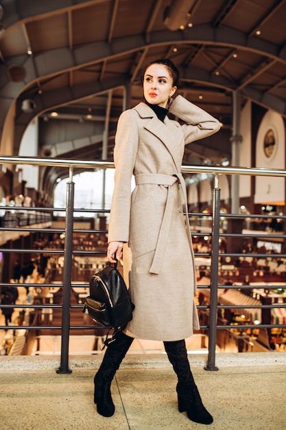 Young woman in long boots and gray coat and holding leather handbag