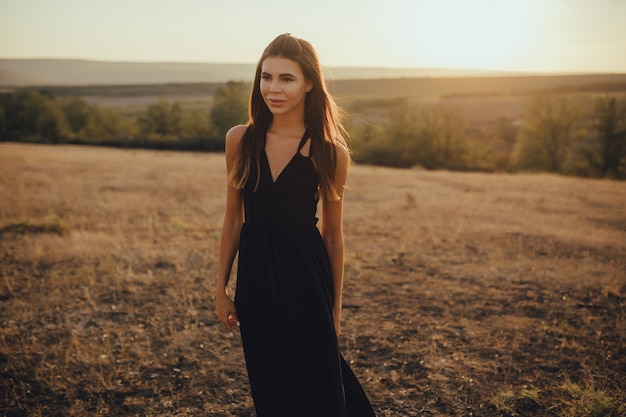 Young woman in long dress enjoying nature on the sunset young lady in elegant black dress 