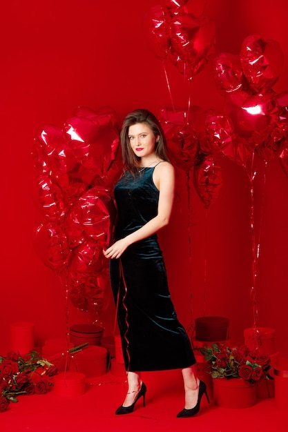 Young woman in long dress with red heart-shaped balloons 