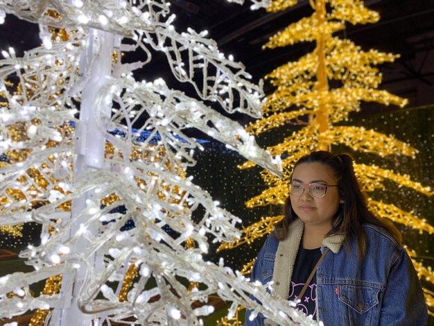 写真 照らされたクリスマスツリーを見ている若い女性