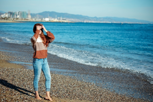 写真 冬のビーチで太陽を見ている若い女性