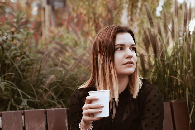 Young woman looking away while drinking coffee against plants