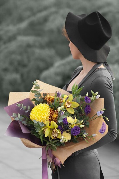 Молодая женщина смотрит в сторону, держа в руках букет цветов на открытом воздухе