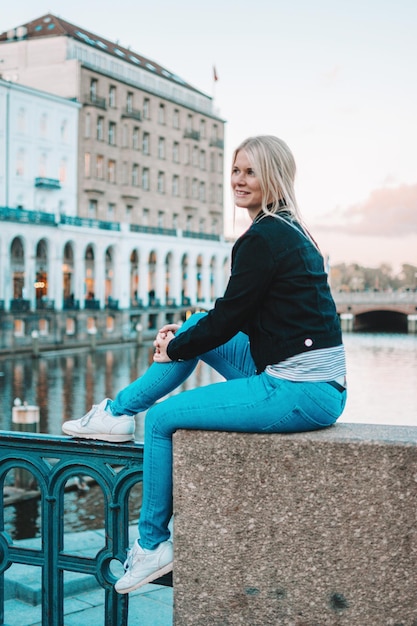 Photo young woman looking away while sitting on railing against sky