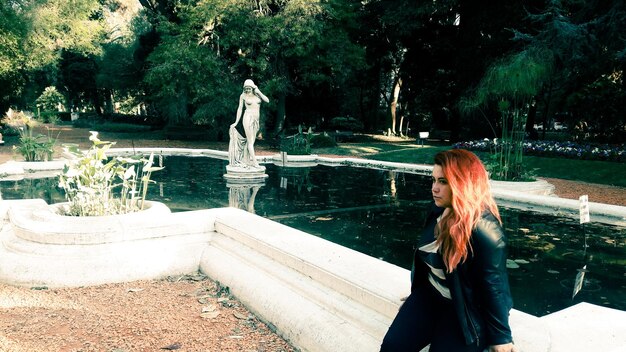 Foto giovane donna che guarda via mentre si trova accanto a una fontana nel parco