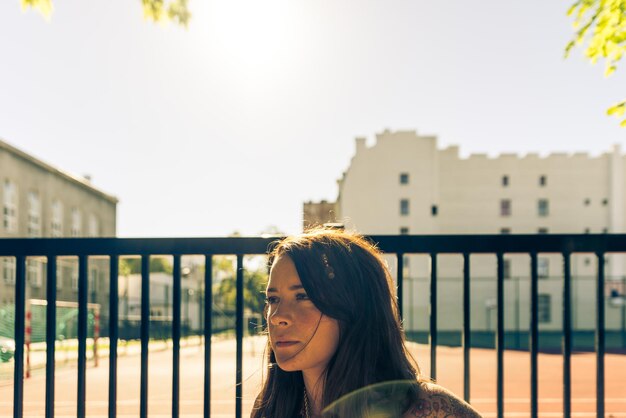 Photo young woman looking away while standing by railing of sport court