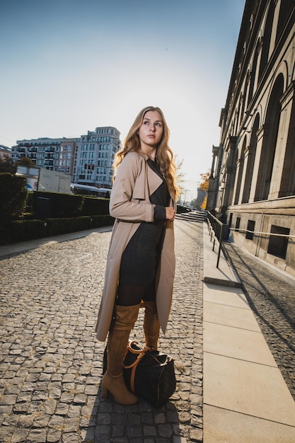 young woman looking away while standing on footpath in city against sky