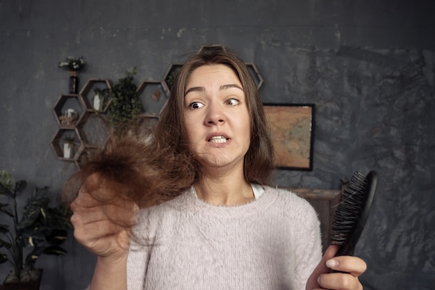 young woman looking on comb with hair, horror and tantrum, hair problems