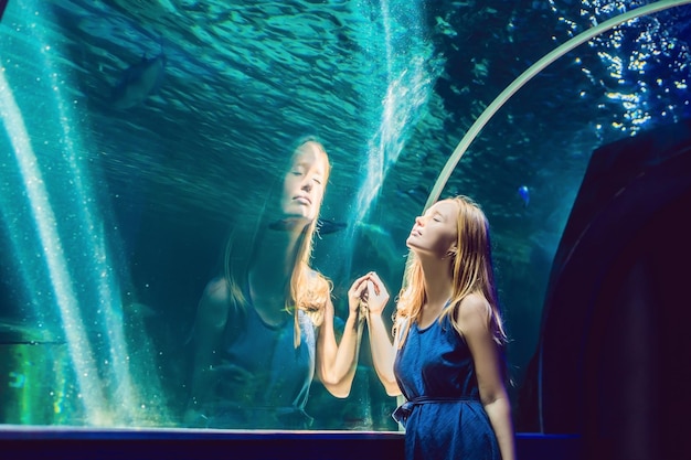 Photo young woman looking at fish in a tunnel aquarium.