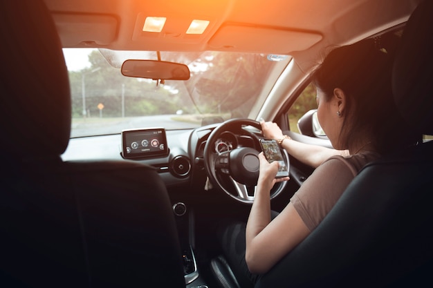 Молодая женщина, глядя на ее смартфон во время вождения автомобиля
