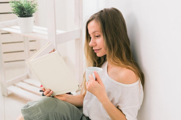 自宅で写真アルバムを探して、お茶の思い出とレジャーの概念を飲む若い女性