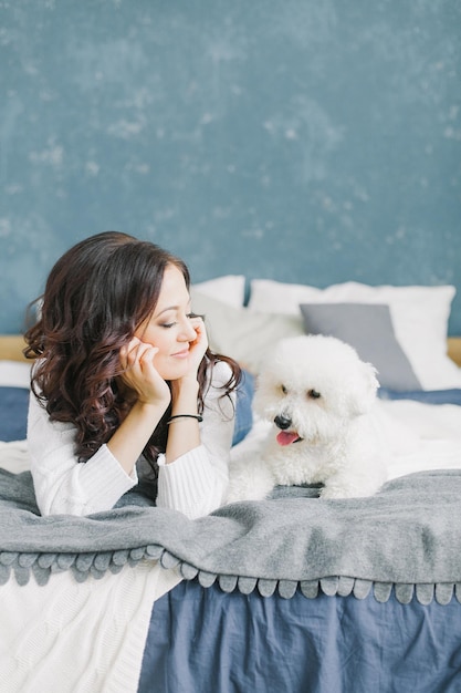 家でベッドに横たわっている若い女性がプードル犬の子犬を見ています